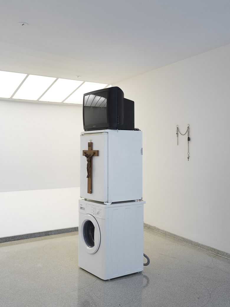 Danh Vo, Oma Totem, 2009. Phillips television set, Gorenje washing machine, Bomann refrigerator, wooden crucifix and personal casino entrance card, 220 x 60 x 60 cm. — © Photo: Nick Ash.